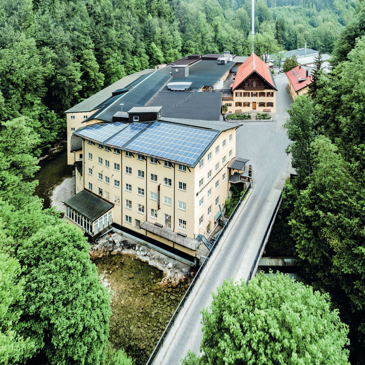 Luftaufnahme des PAPIERWELT Industriekomplexes mit Solardächern an einem Fluss, umgeben von Wald.