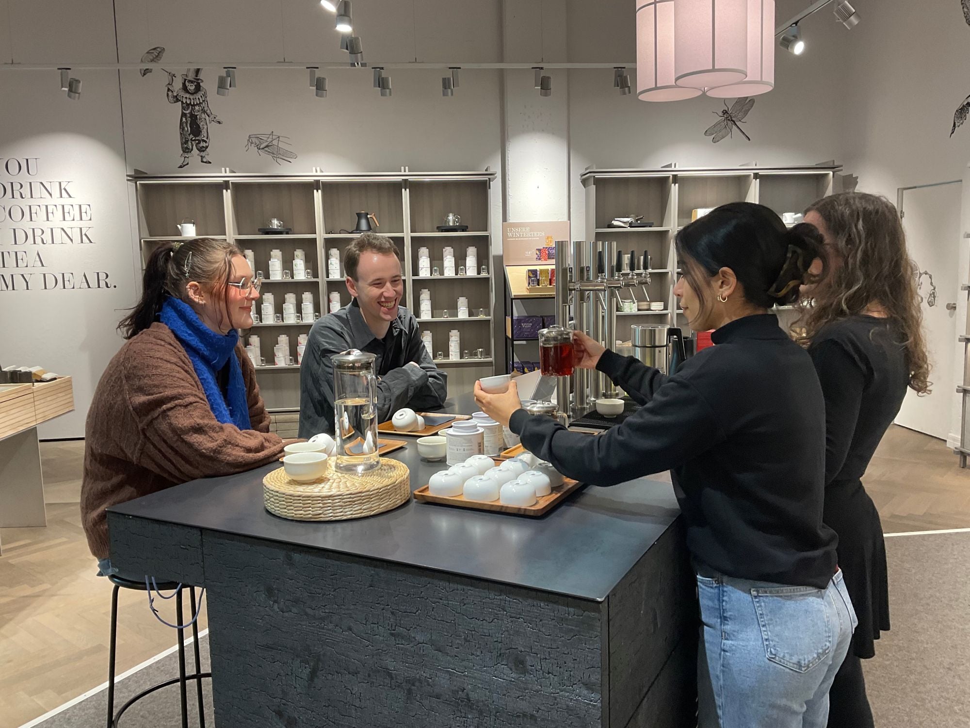 Vier junge Erwachsene trinken roten Tee an einem schwarzen Tisch in einem modernen Teegeschäft.