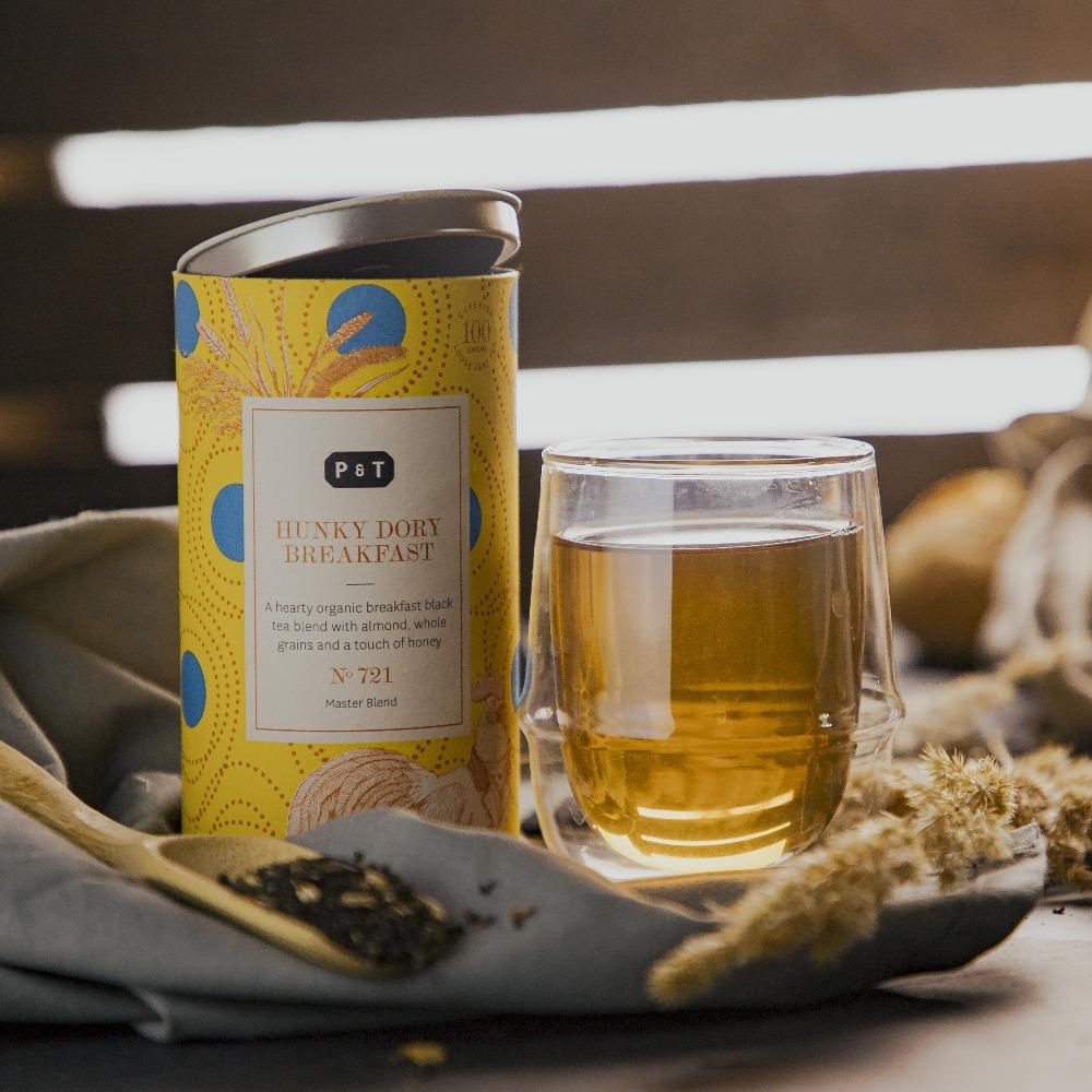 Gelbe Teedose von P & T HUNKY DORY BREAKFAST, Glastasse mit Bernsteintee, Holzlöffel mit losem Bio-Schwarztee.