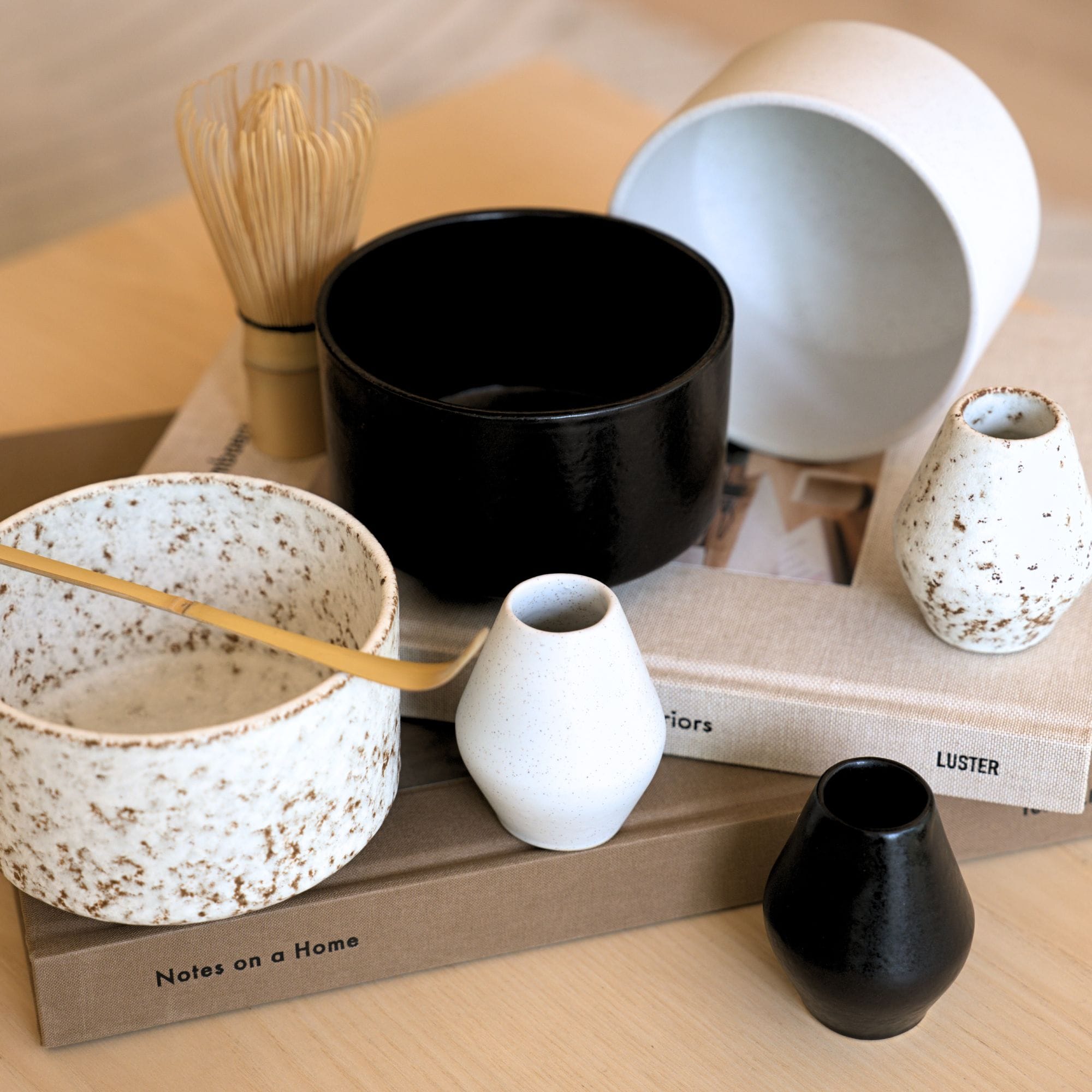 Keramikschalen, Vasen und Bambusbesen auf Büchern, stilvolles Interieur-Arrangement.