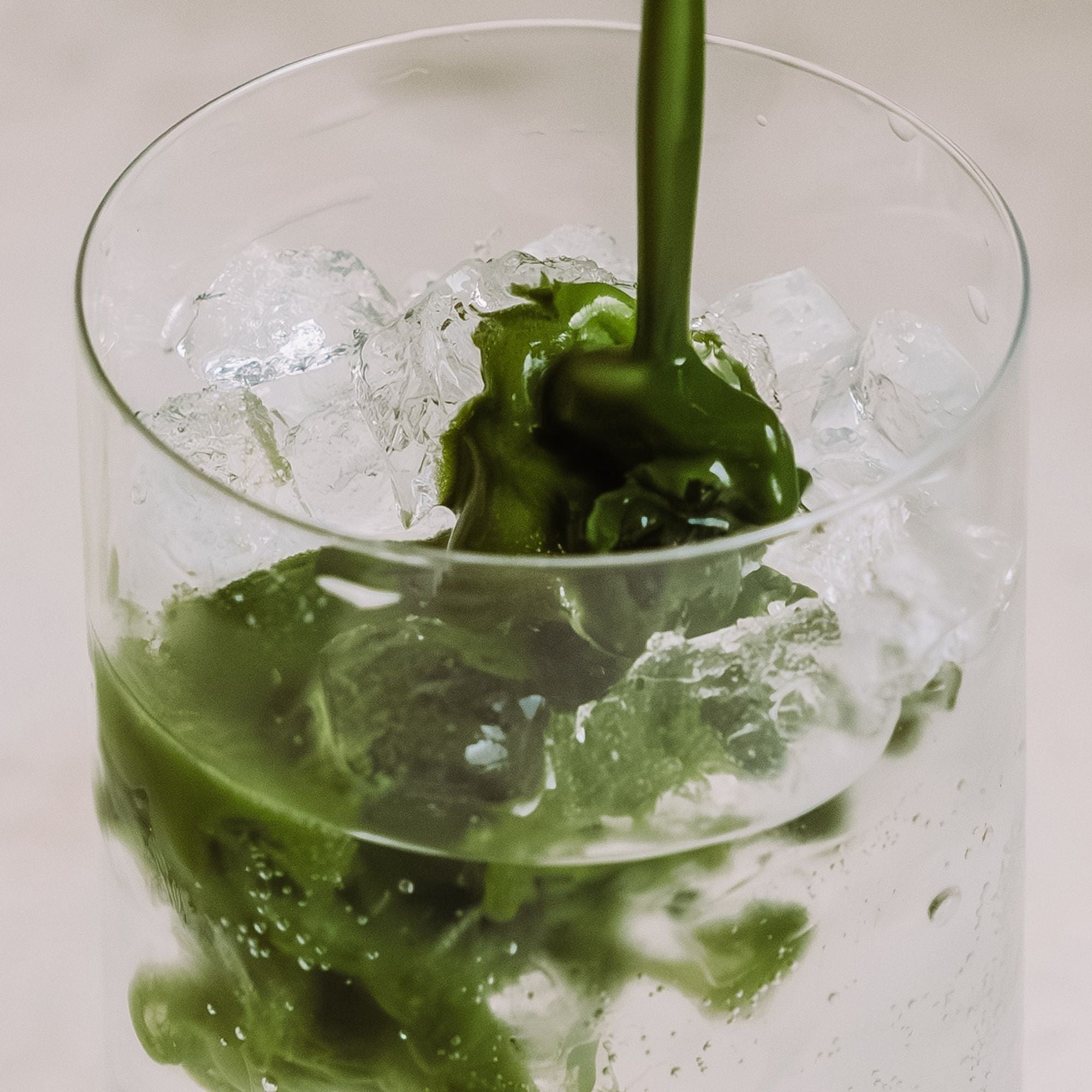 Klares Glas mit Eiswürfeln, in das grüne Teeflüssigkeit von P&T eingegossen wird.