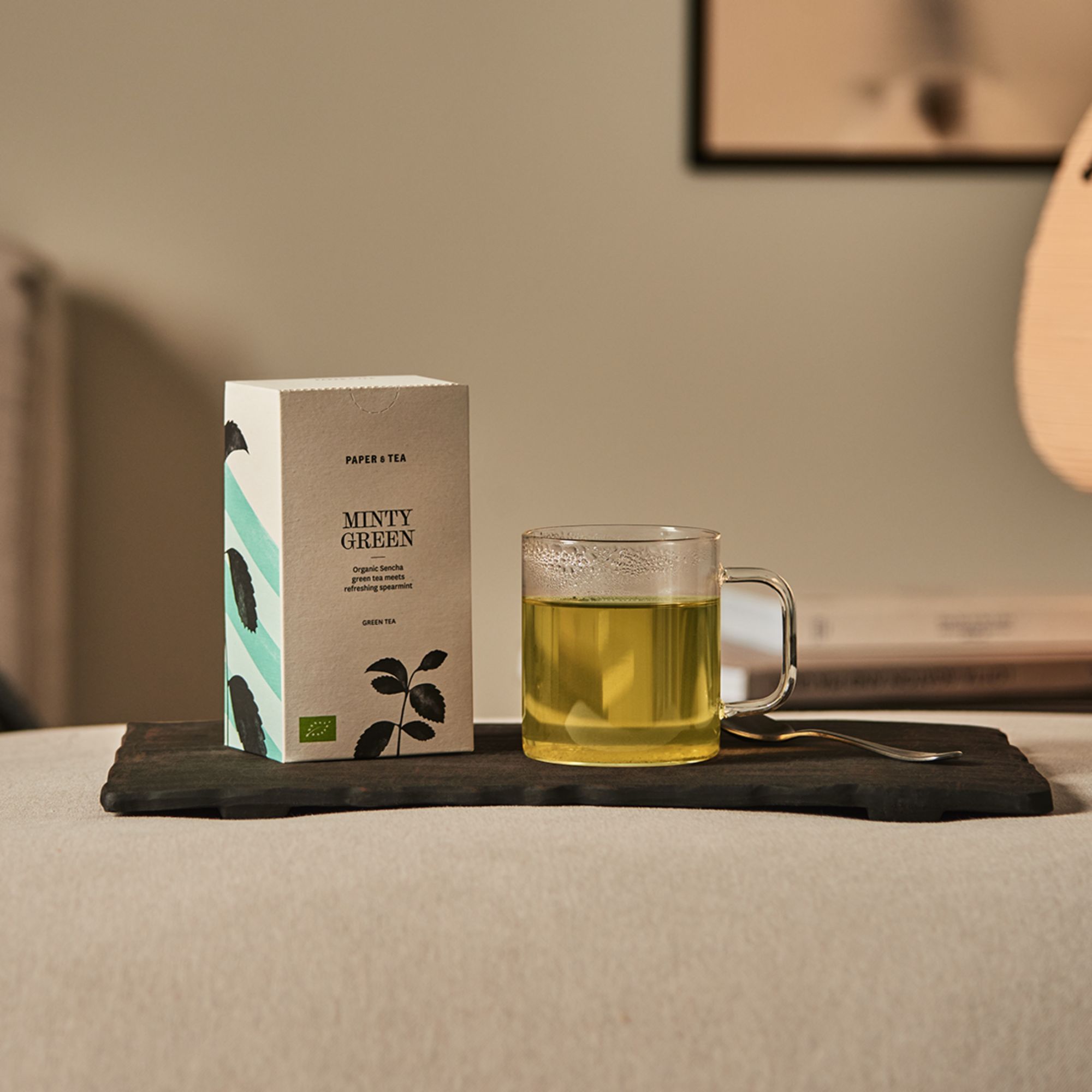 Paper & Tea Minty Green Verpackung mit Bio-Sencha-Grüntee und Minze neben Glas mit grünem Tee auf Holztablett