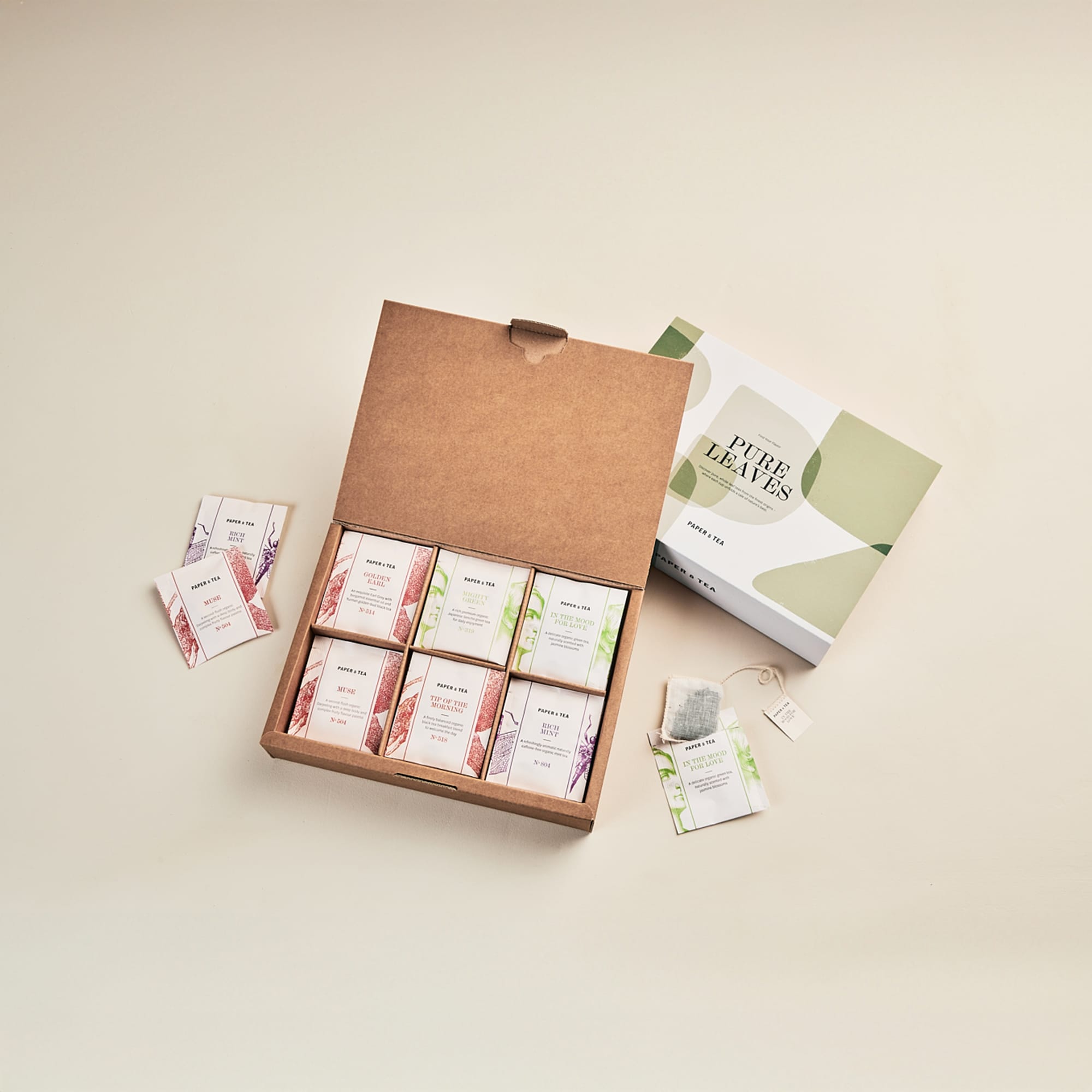 Offene braune Schachtel mit sechs Paper & Tea Teeboxen, zwei losen Teepäckchen, PURE LEAVES Schachtel, IN THE MOOD FOR LOVE Beutel.