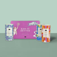 Lila Schachtel mit weißem Pferd und 'KISS IT BETTER', zwischen bunten Zylindern mit Muster und Schokoladentext.