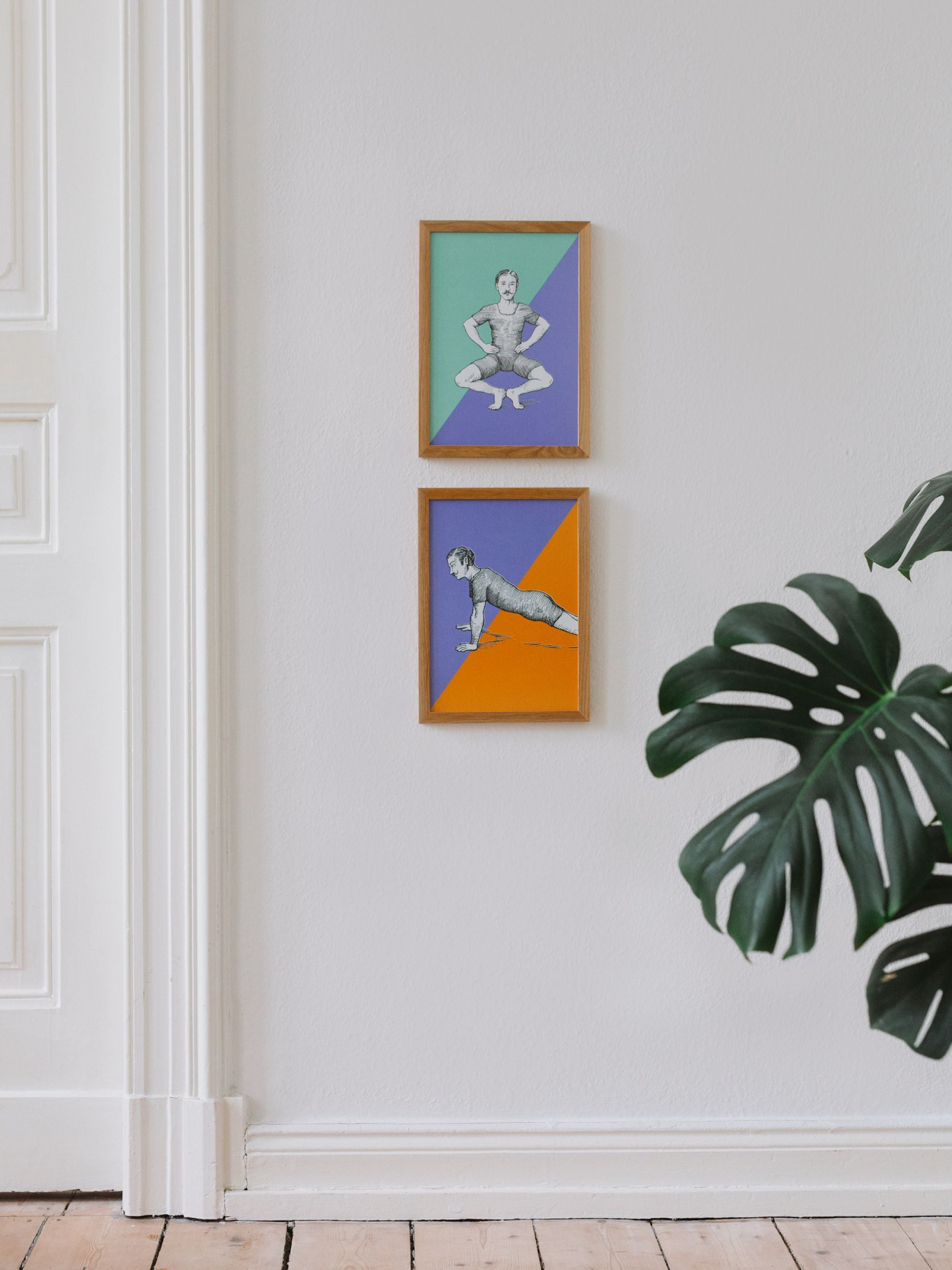 Zwei hängende Holzrahmen mit Vintage-Illustrationen von turnenden Männern, bunten Hintergründen und Monstera-Blättern.
