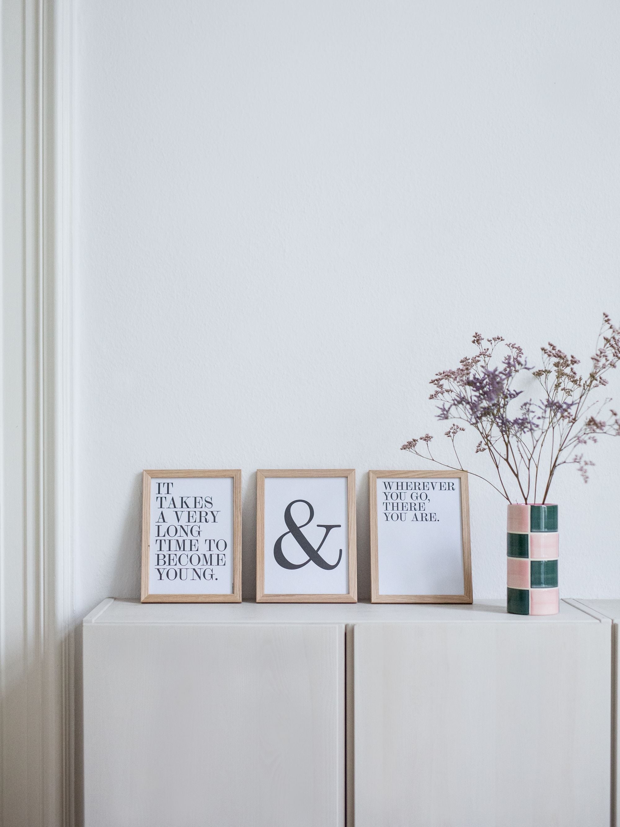 Minimalistisches Interieur mit Holzrahmen, inspirierenden Texten und einer Keramikvase auf einem Sideboard.