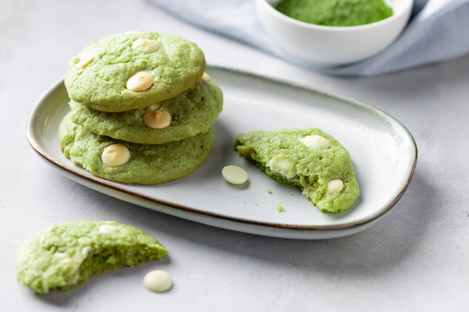 Drei grüne Matcha-Kekse mit weißen Schokoladenstückchen auf einem Teller