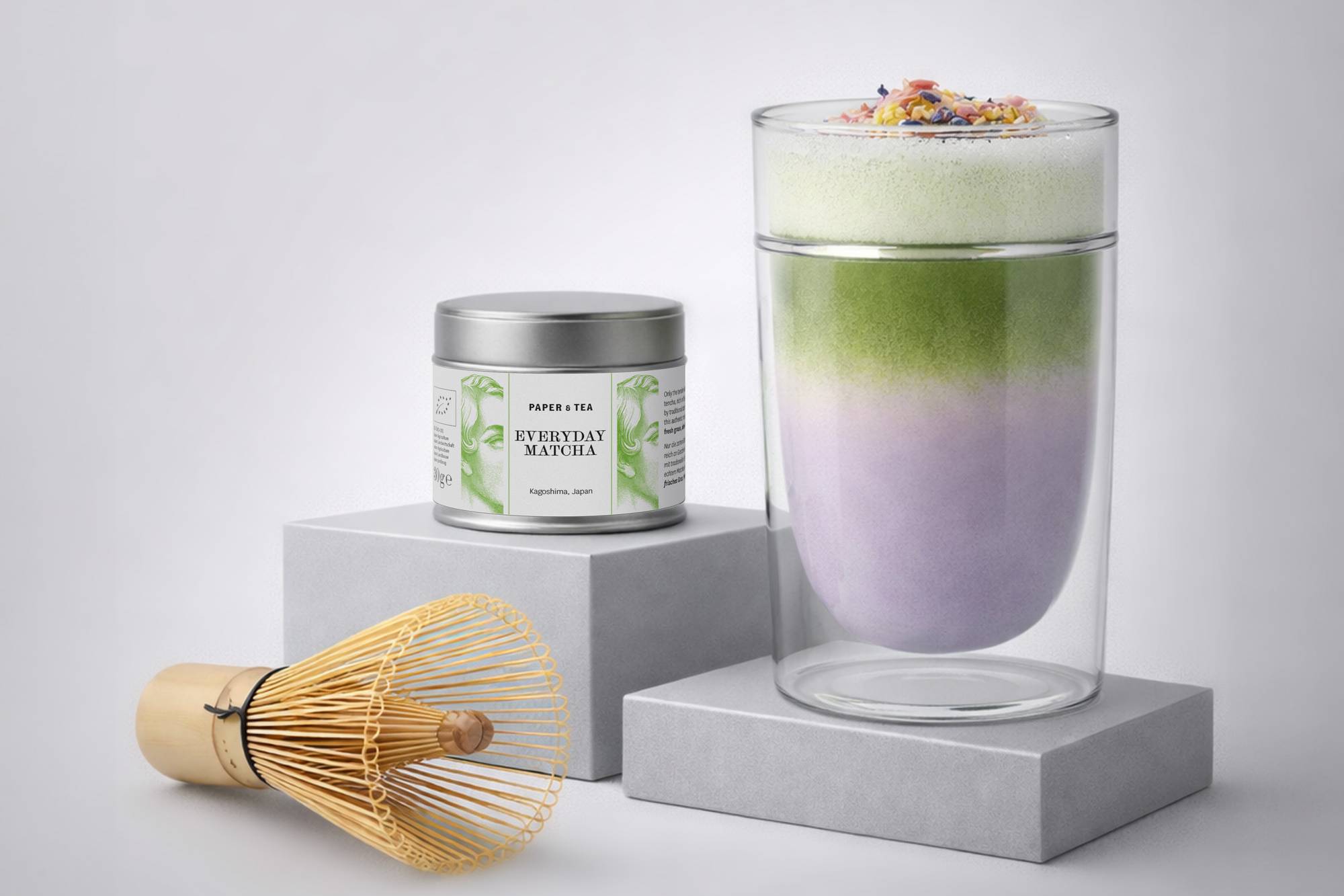 Doppelwandiges Glas mit grün-weiß-lila geschichtetem Matcha-Getränk und Blüten