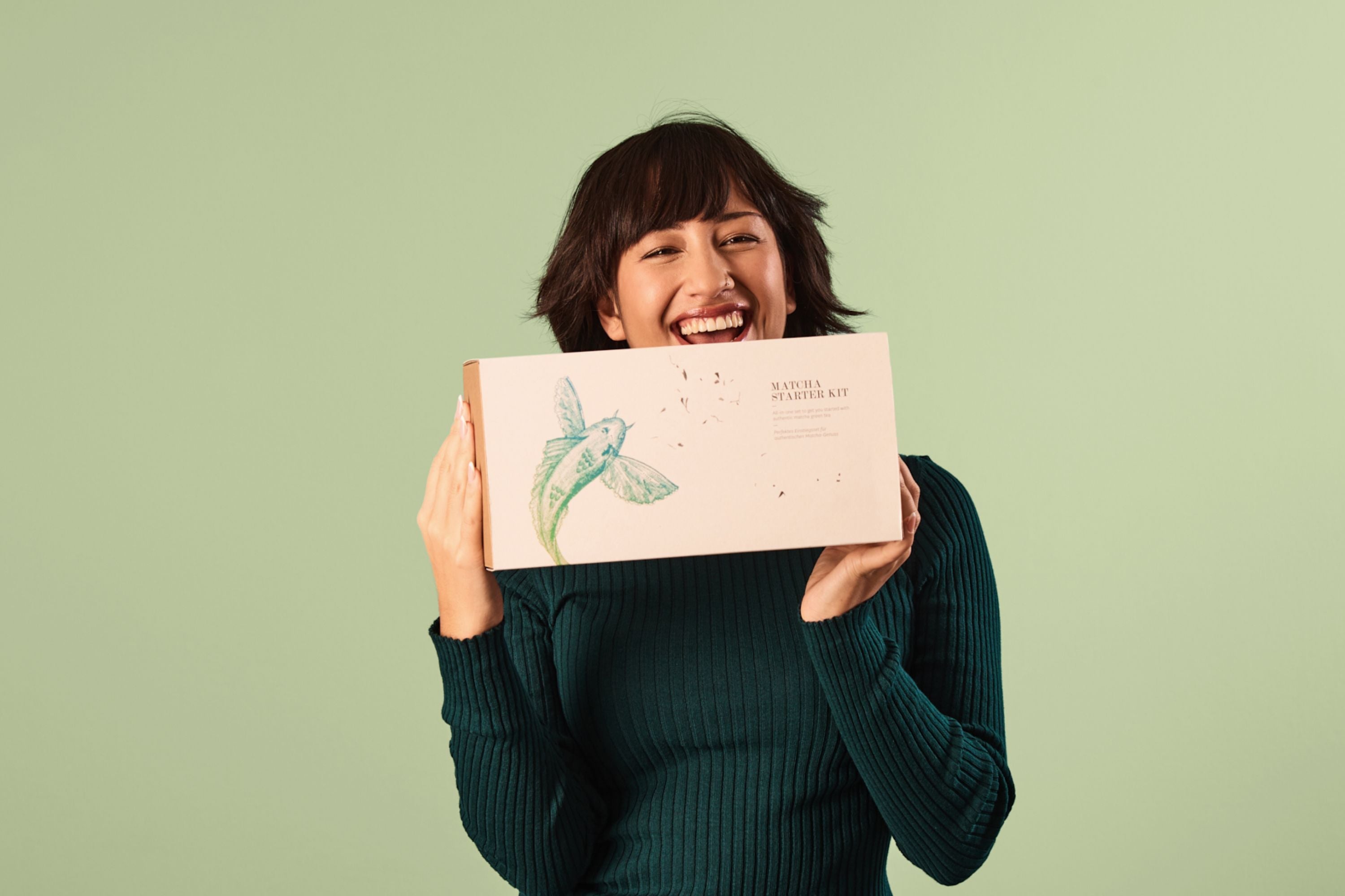 Person in hellem, geripptem Pullover hält drei Teedosen vor einem hellgrünen Hintergrund