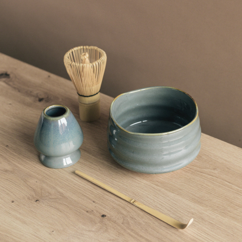 Traditionelle japanische Teezeremonie-Utensilien auf hellem Tisch mit Keramikschälchen und Bambusbesen.