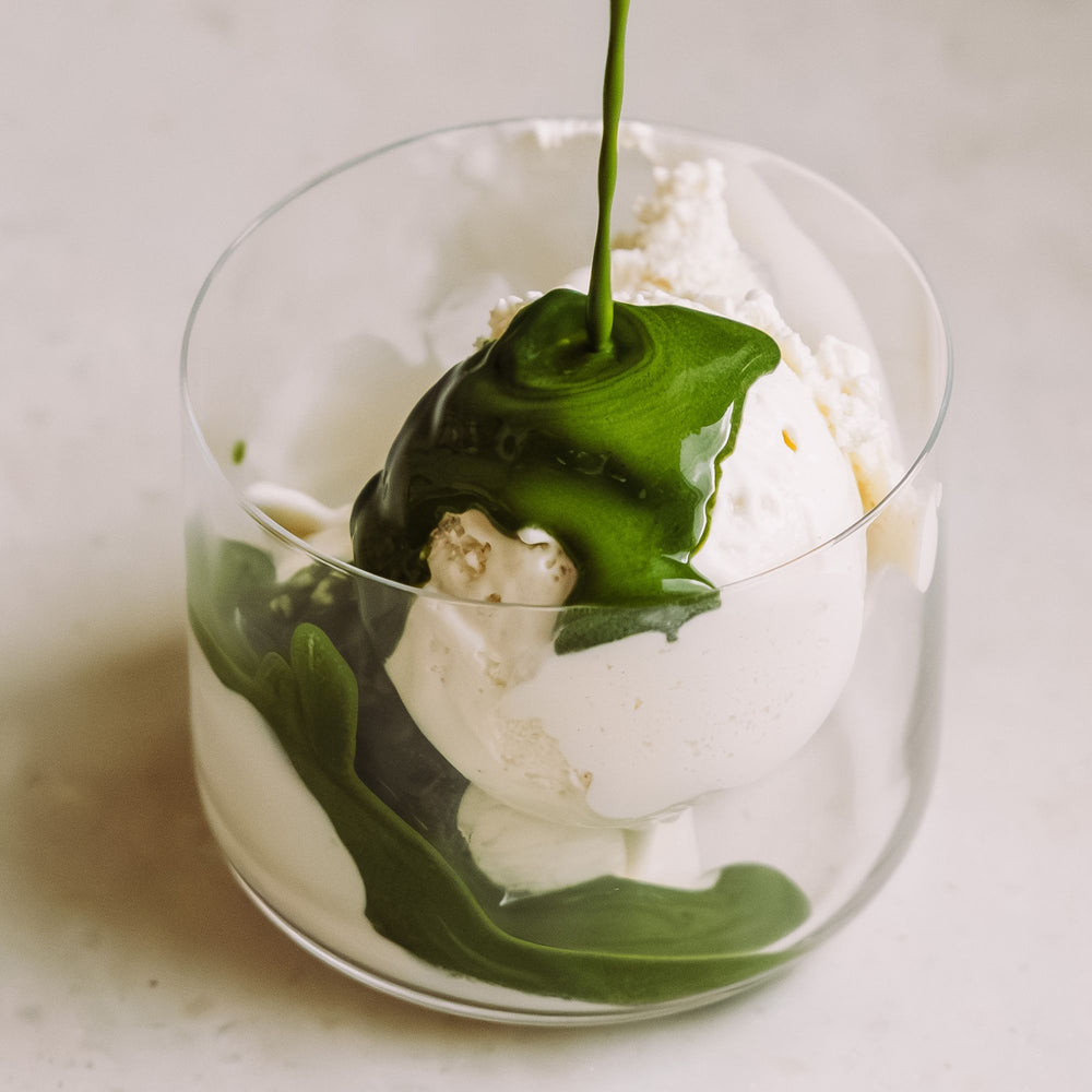 Ein transparentes Glas mit weißen Eiskugeln, über die eine grüne Sauce gegossen wird.