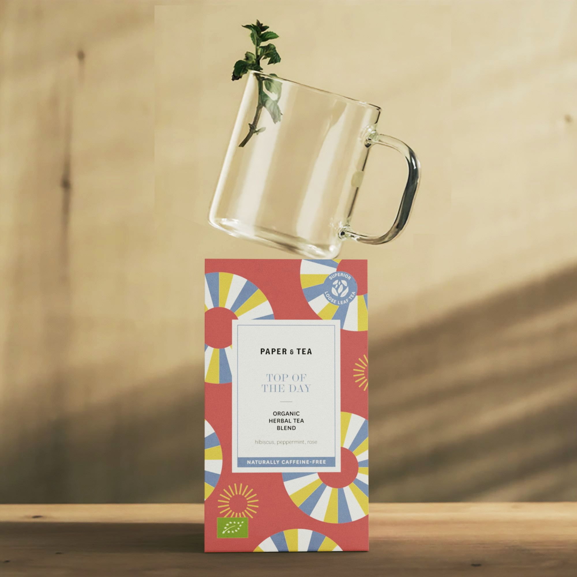 Bunte Papierschachtel mit BIO-Kräutertee-Mischung, Hibiskus, Pfefferminze, Rose neben Glas Minze.