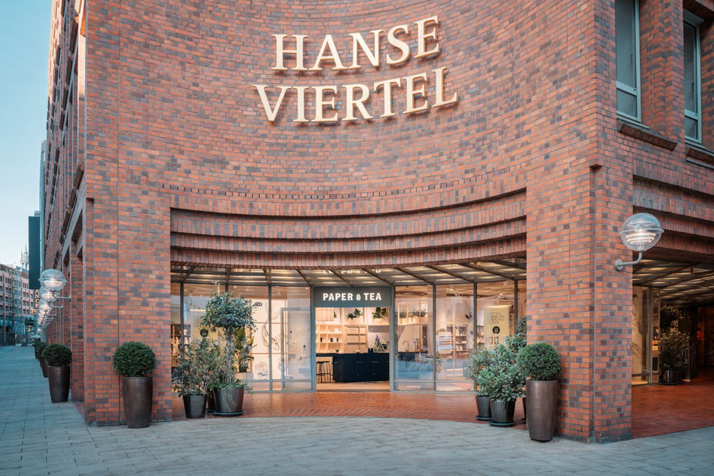 Geschwungene Backsteinfassade des Hanse Viertels mit P&T Teeladen und grünen Pflanzen am Eingang.
